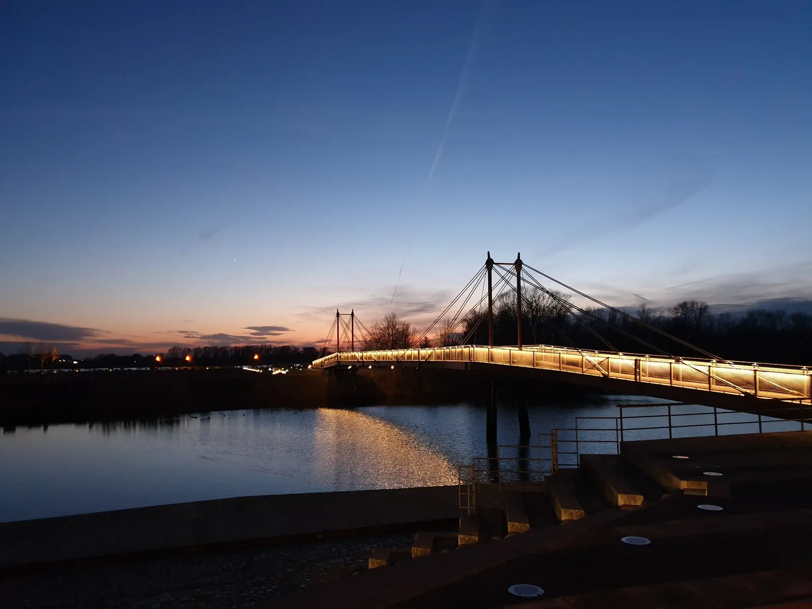 Beleuchtete Fußgängerbrücke über dem Wasser in der Abenddämmerung